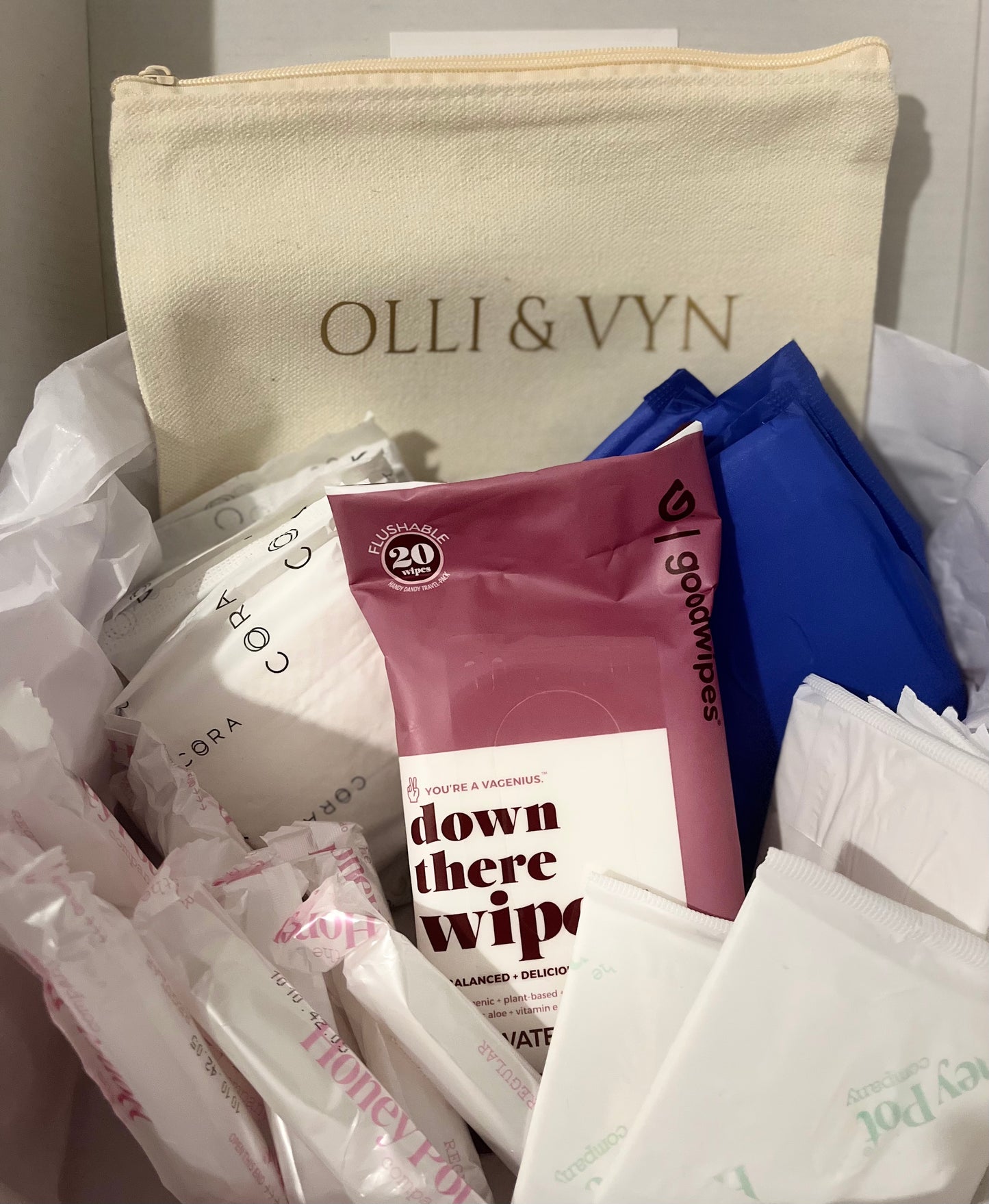 period kit with period pads, tampons, liners and wipes. off white period kit bag with company's name in gold