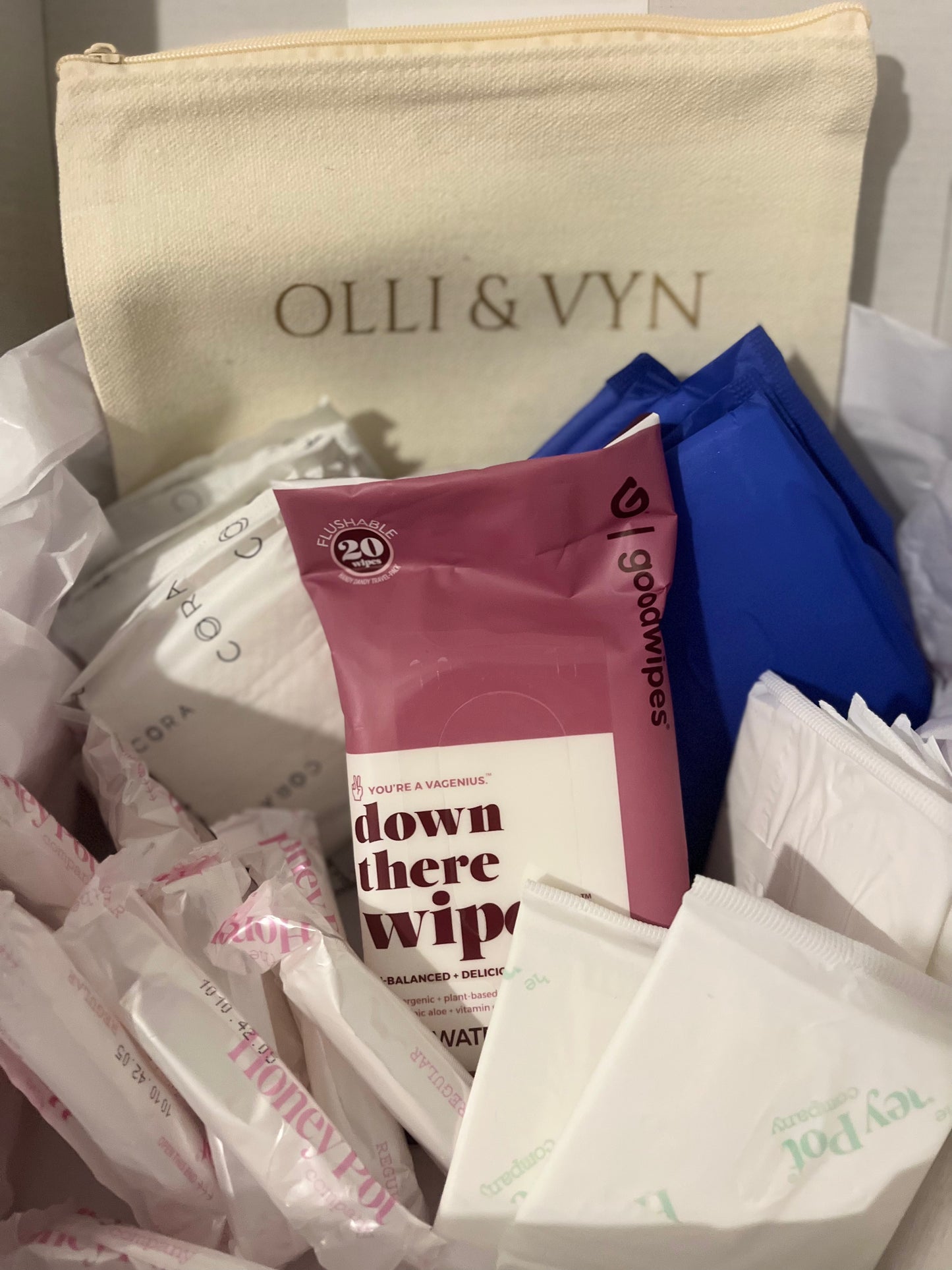 period kit with period pads, tampons, liners and wipes. off white period kit bag with company's name in gold