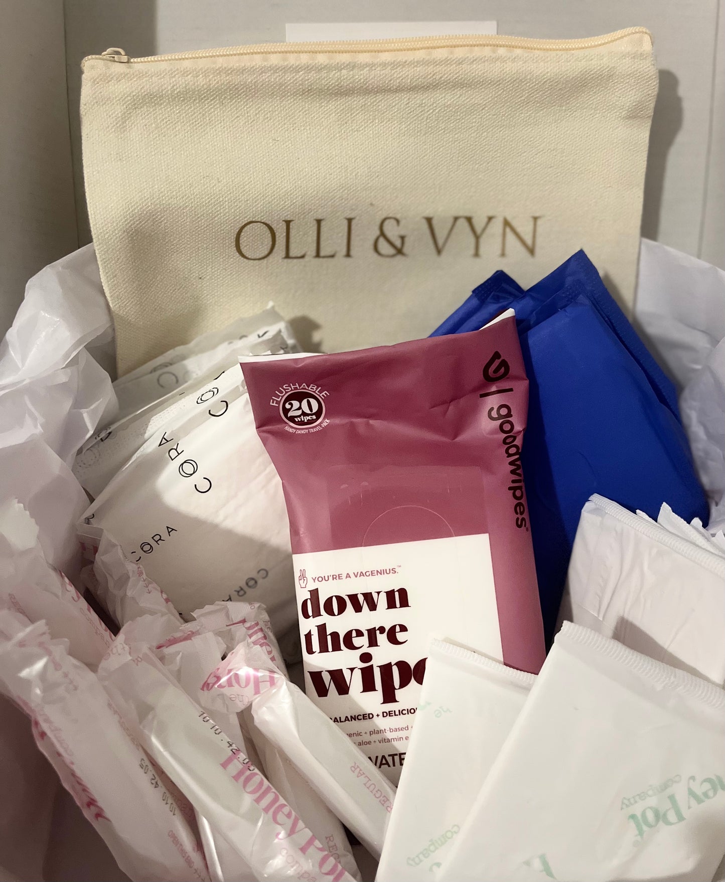 period kit with period pads, tampons, liners and wipes. off white period kit bag with company's name in gold