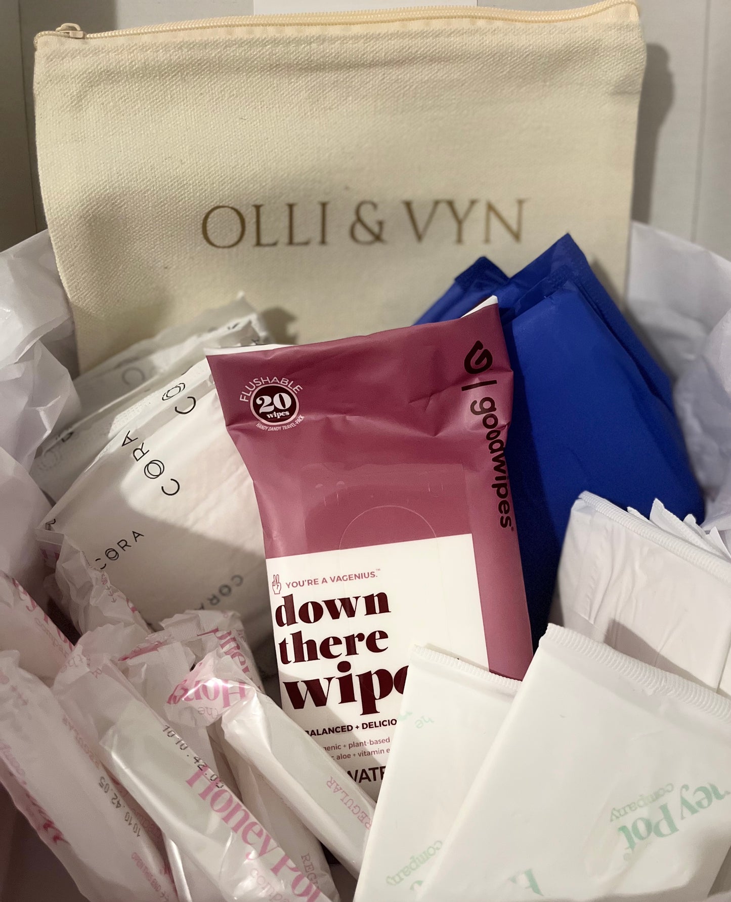 period kit with period pads, tampons, liners and wipes. off white period kit bag with company's name in gold