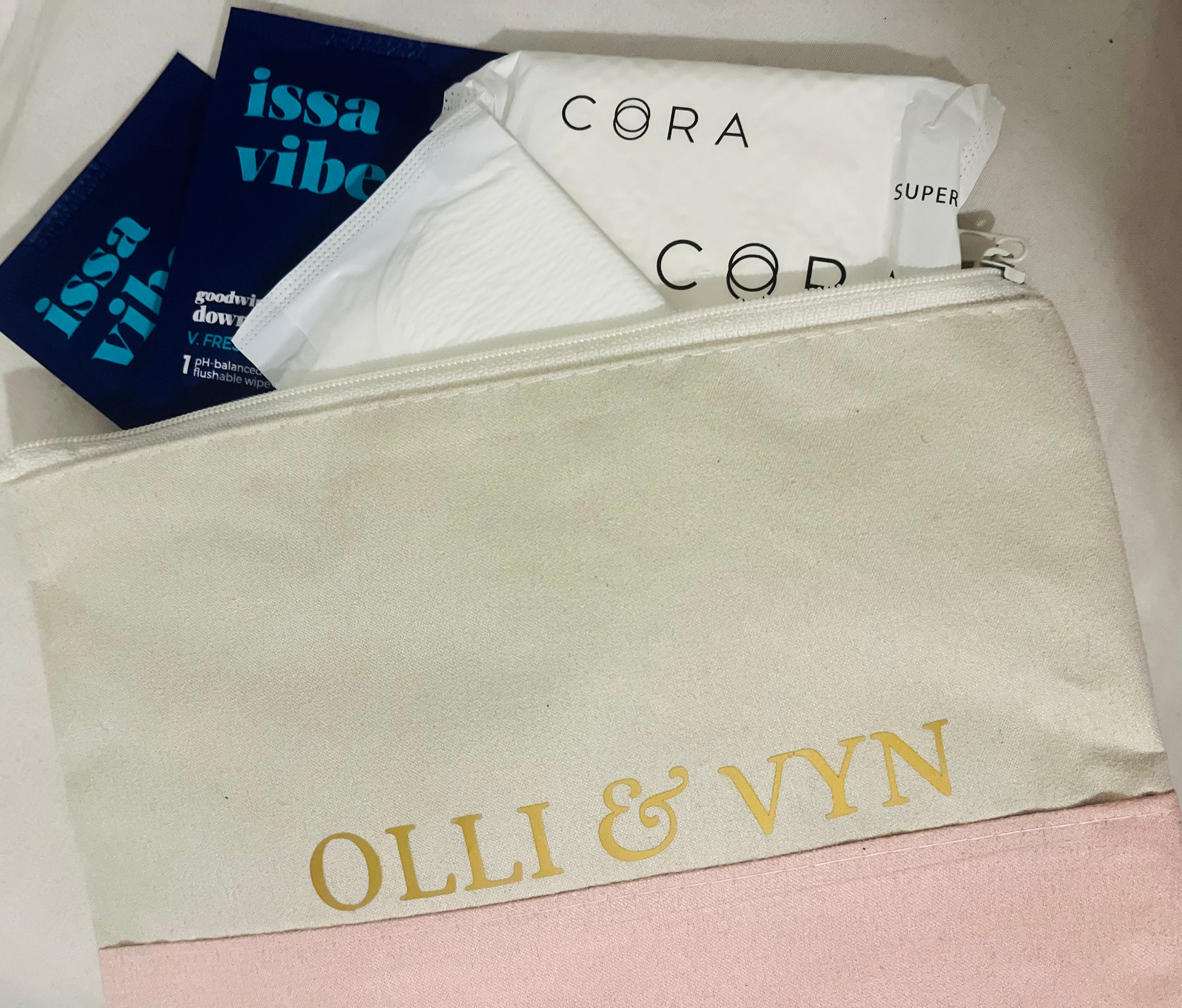 off white and pink suede period kit bag with company name in gold. period kit products including period pad, wipes and period liner